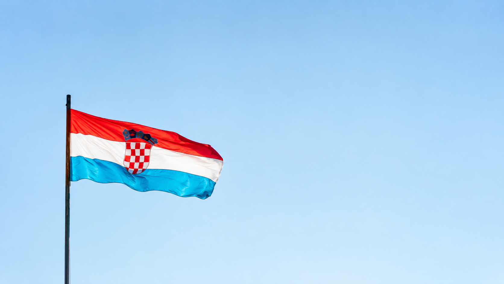 Hrvatska zastava na jarbolu ispred vedrog neba.